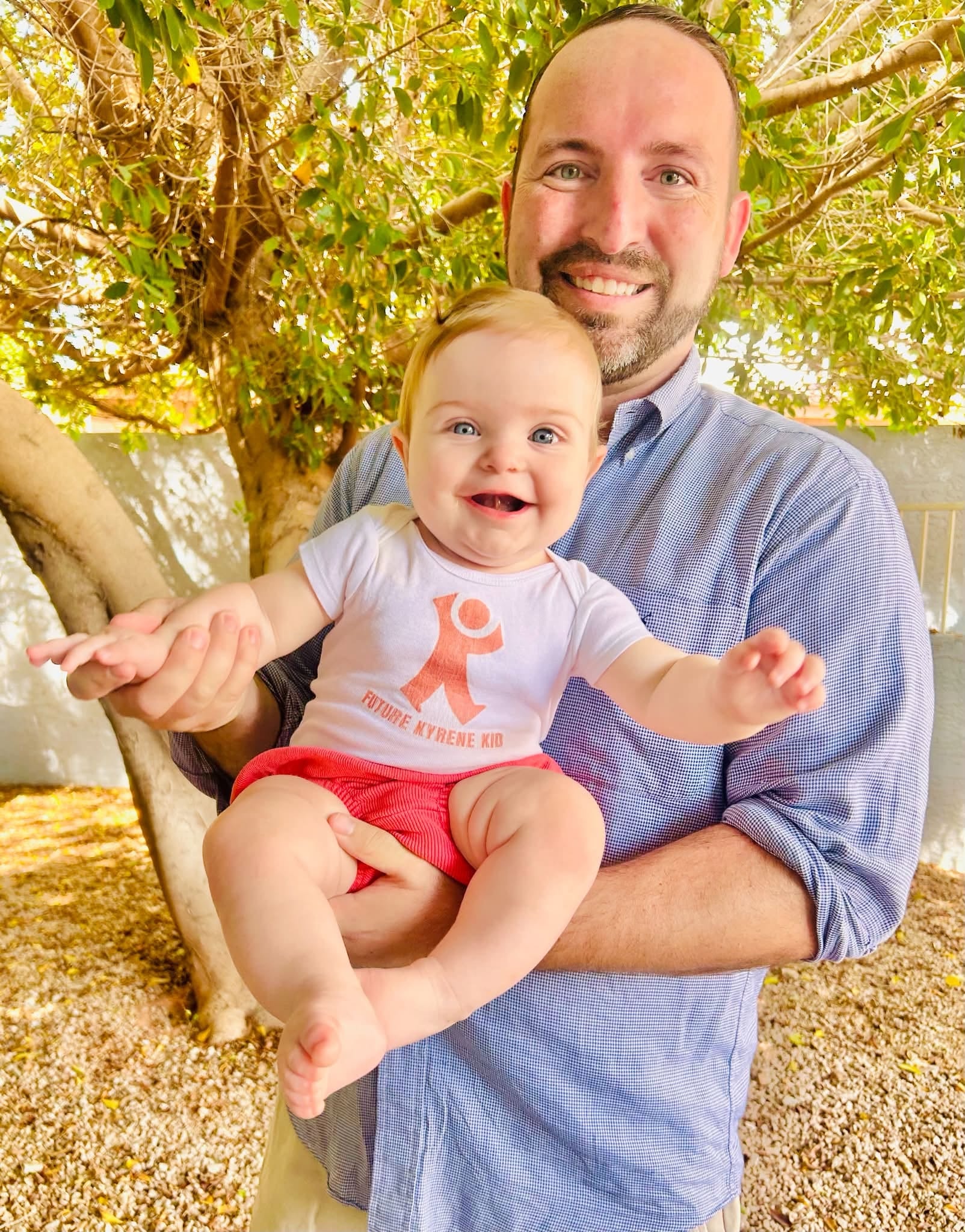 Kevin Walsh holding a baby in a Future Kyrene Kid onesie